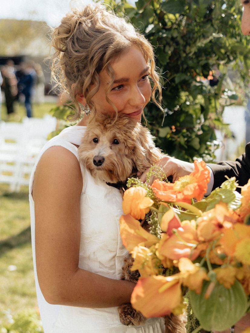 Bride with a romantic curly updo and face-framing tendrils holding her dog